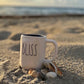 Jacqueline collecting shells in her coffee cup on beach  jacqueline mb designs 